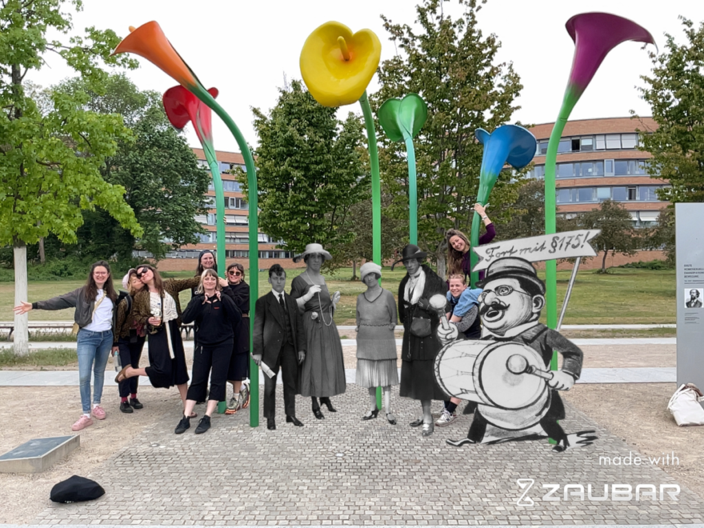 A group of people stand laughing at the memorial of the world's first queer emancipation movement in Berlin. In their midst are queer people in Augmented Reality from the 1920s.